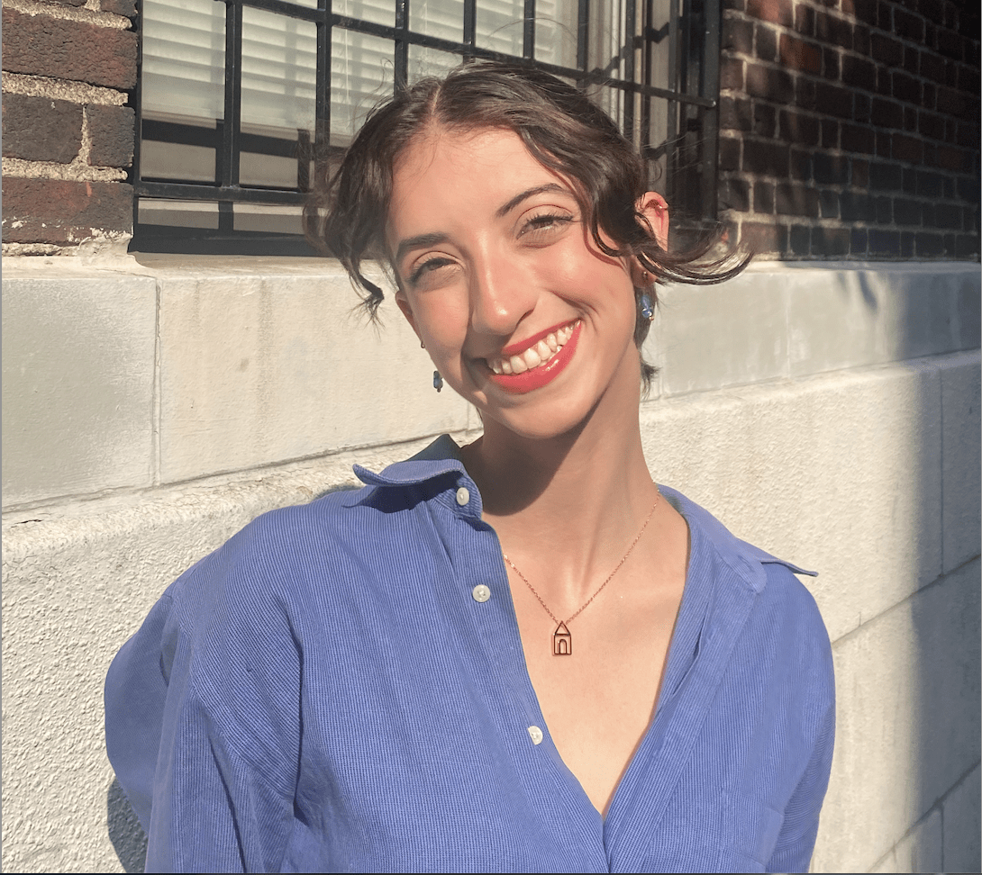 Stephanie a mixed race white passing young woman smiles in warm sunlight. She wears a blue button down.